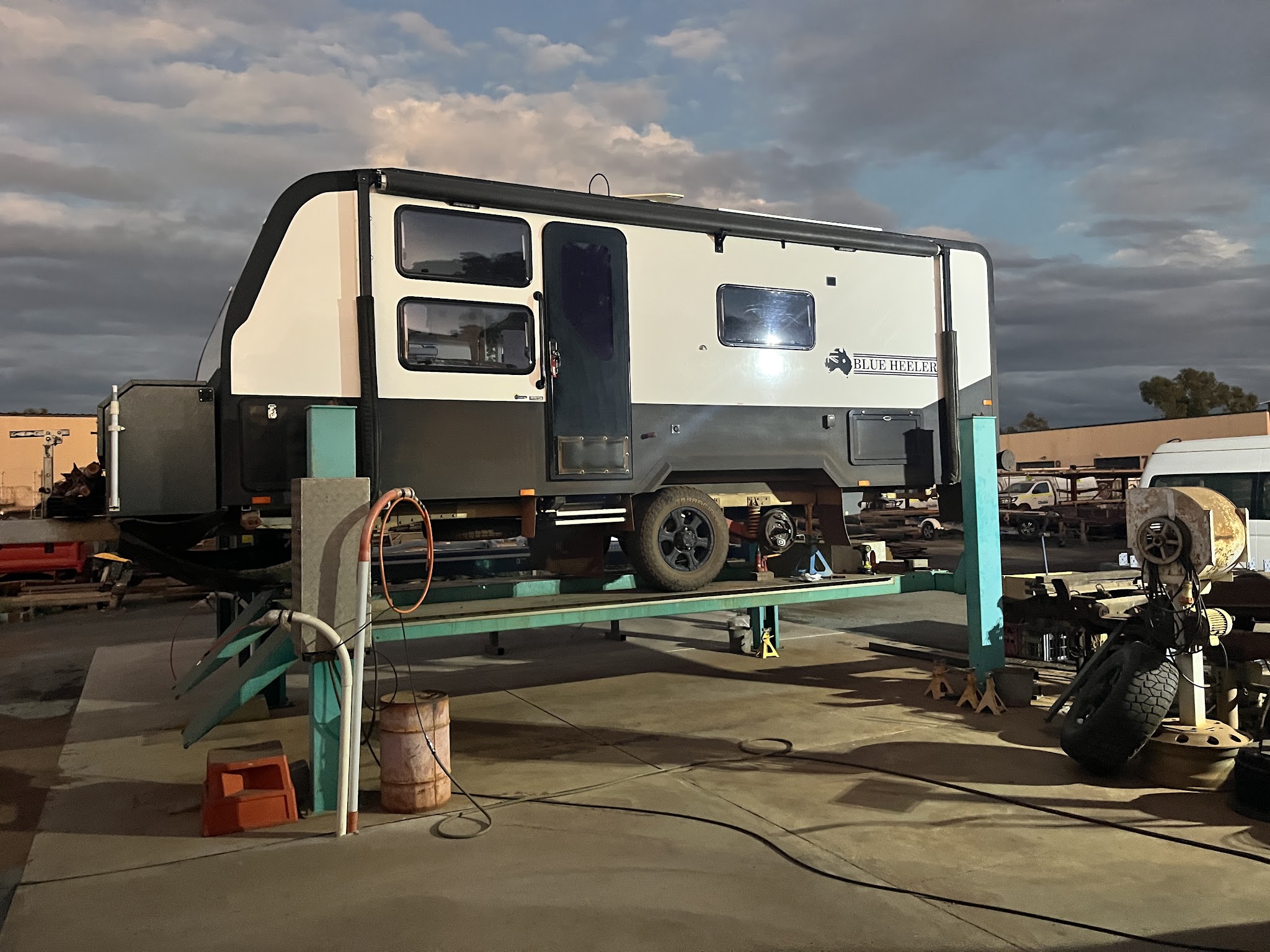 A hybrid off-road caravan lifted on the hoist in the J.K'S Aluminium yard at dusk